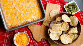 Cheesy dip with tortilla chips and toppings on a red checkered tablecloth