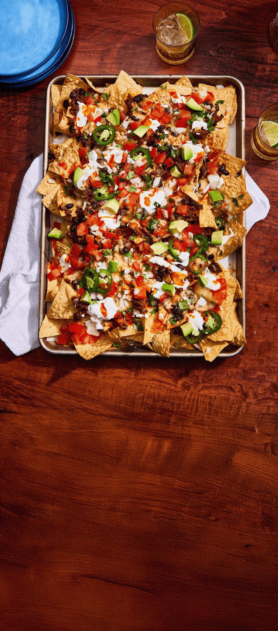 Sheet pan of loaded nachos with various toppings on a wooden table.