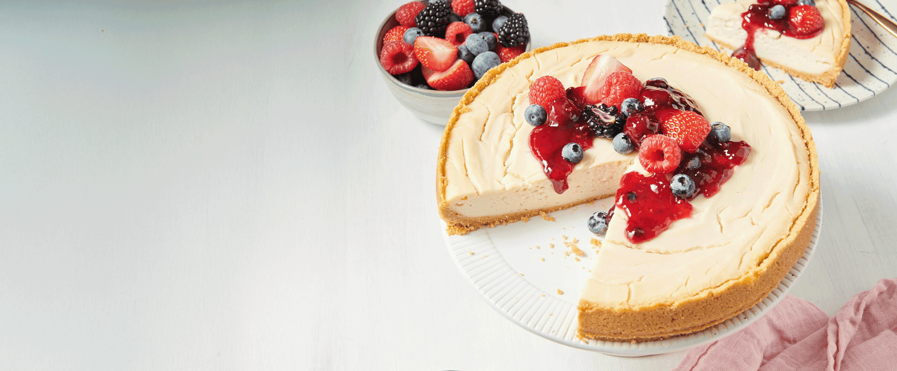 Cheesecake with berry toppings on a white plate, surrounded by more berries.