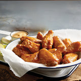 Glazed buffalo chicken wings served in a white bowl with dipping sauce and lime wedges on the side.