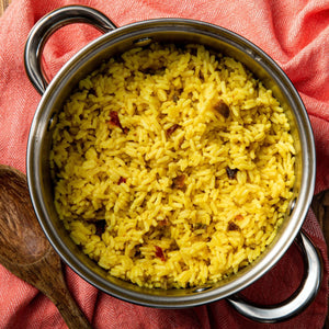 A pot of yellow rice with a wooden spoon on a red and white patterned cloth.