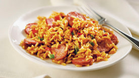 Plate of yellow rice with sausages and vegetables on a white plate.