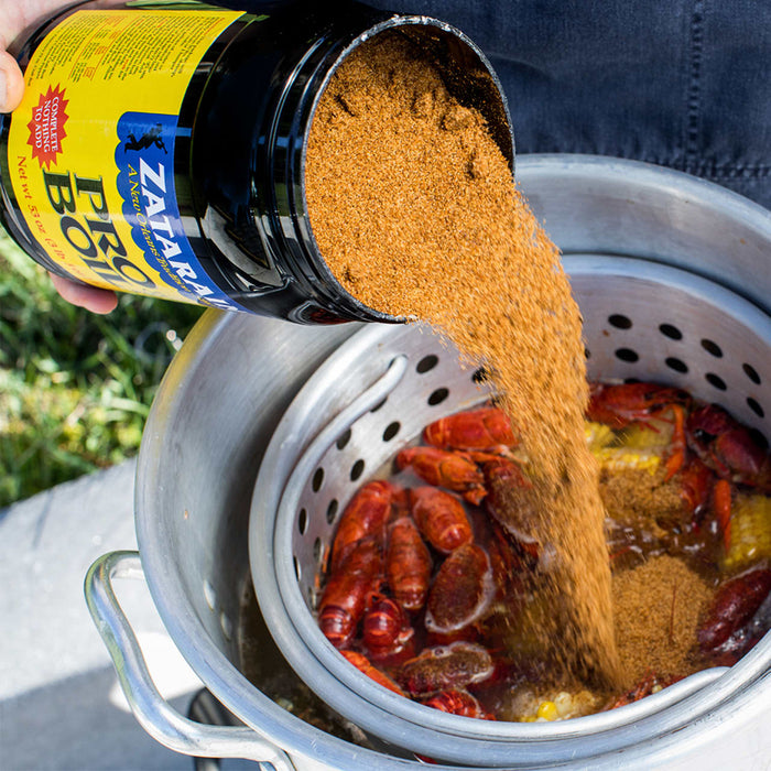 A hand pours Zatarains Pro Boil seasoning into a pot of crawfish.